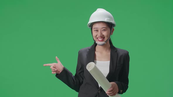 Smiling Asian Female Engineer Holding Blueprint And Pointing To The Side In The Green Screen Studio