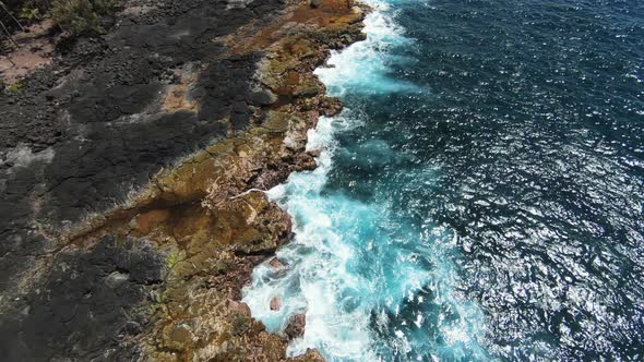 FPV slomo aerial rise above blue ocean crashing against orange basalt shoreline