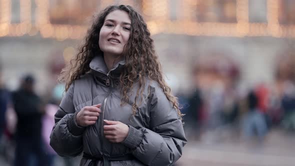 A Young Smiling Woman with Curly Hair Poses on a City Street Wearing a Jacket Cold Season