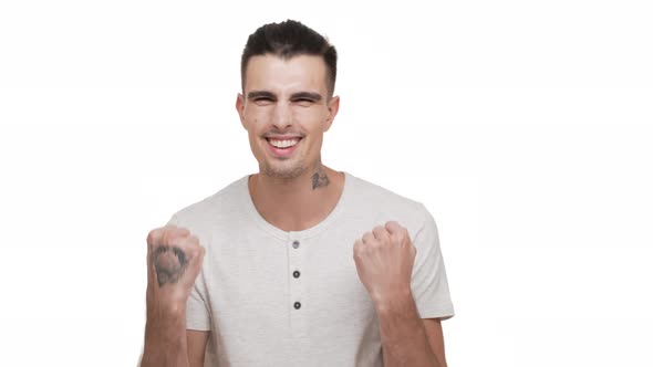 Horizontal Portrait of Brunette Tattooed Guy Wearing White Shirt Being Happy Clenching Fists Smiling