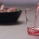 Slow Motion Pour Pink Fizzy Drink in a Tumbler Glass on Walnut Table with Salad on Background - VideoHive Item for Sale