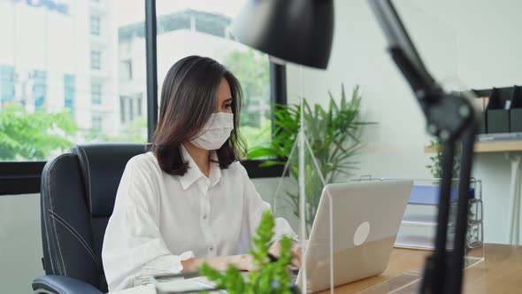 Asian young business woman wear mask working on a computer in the office with a new normal lifestyle