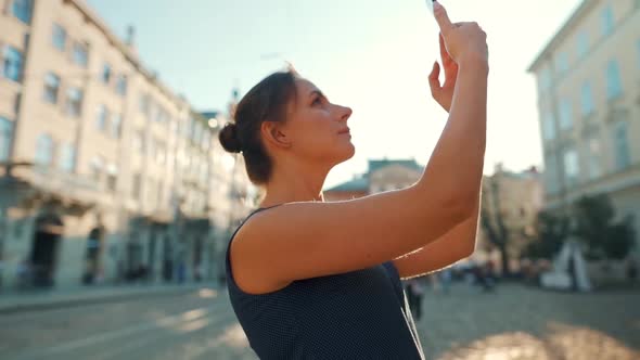 Woman Stands on an Old Street and Takes a Photo or Video on a Smartphone at Sunset. Slow Motion