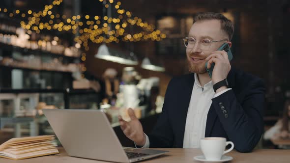 Businessman Sitting at the Cafe Talking on Smartphone and Smiling While Having Phone Conversation