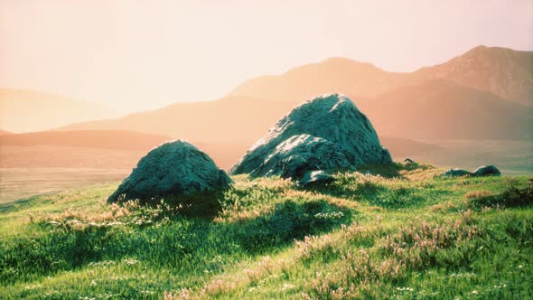 Meadow with Huge Stones Among the Grass on the Hillside at Sunset