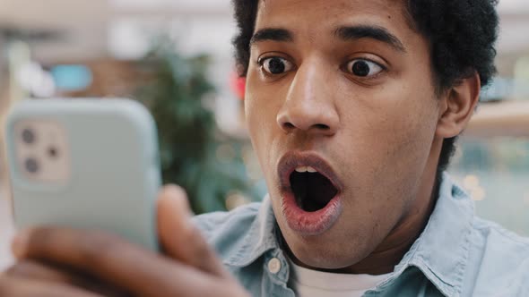 Closeup Portrait Shocked African American Millennial Man Open Mouth in Shock Looking at Smartphone