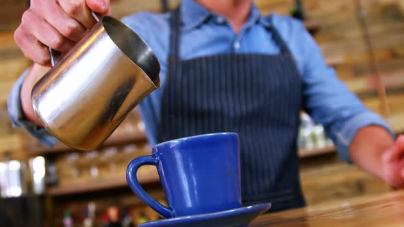 Waiter pouring milk in coffee at counter