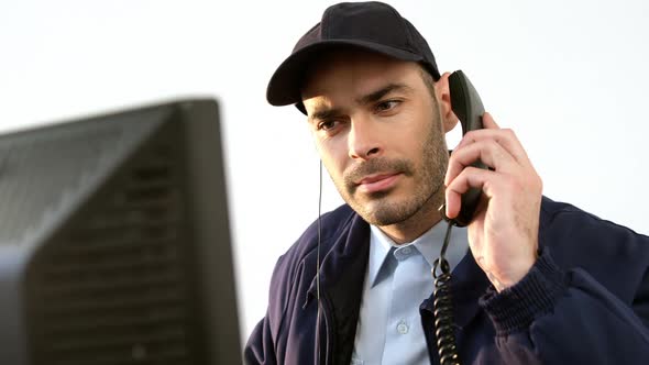 Security guard talking on phone while working on computer