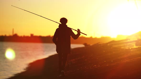 A Fisherman Walks Along the City Shore Against the Backdrop of a Beautiful City Sunset