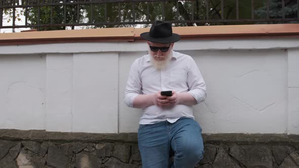 Old Man with Albinism Browsing on the Internet While Sitting Next To His House