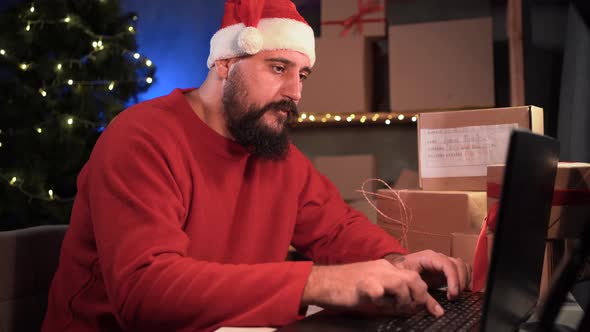 Hindu Salesman in Santa Claus Costume Confirming Orders From Customer Using Laptop