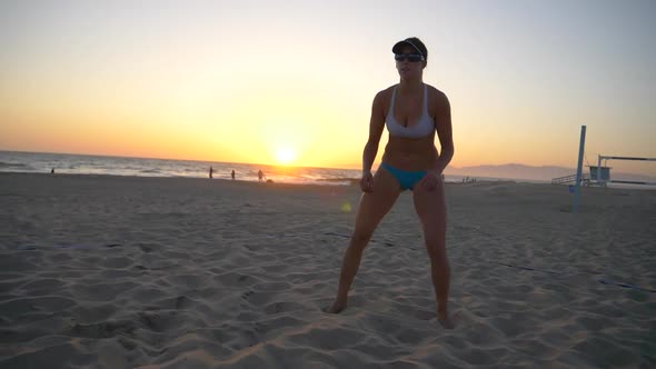 Women players play beach volleyball and a player digs the ball.