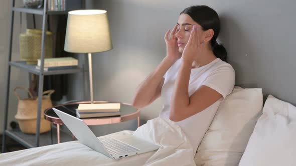 Young Latin Woman with Laptop Having Headache in Bed