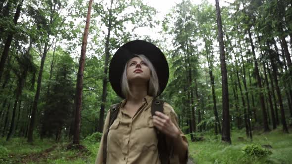 Blonde woman in hat with backpack in rainy forest