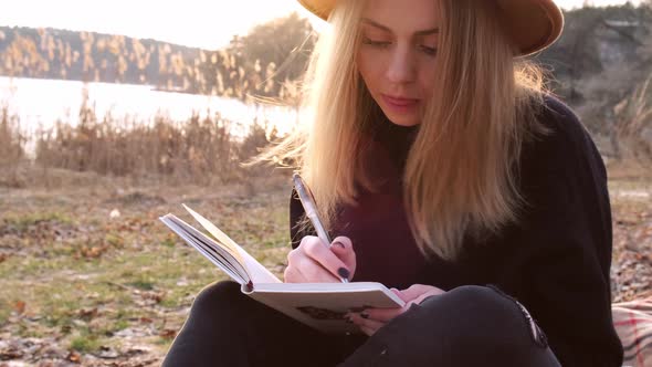 Caucasian Blonde Woman with Beige Hat in Black Sweater Write on Notebook in the Countryside