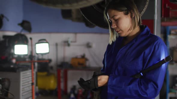 Female mechanic holding led lamp wearing protective gloves at a car service station