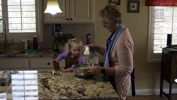 Grandmother mixing cake batter with granddaughter toddler helping