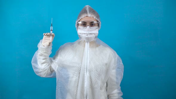 Young Woman in a Protective Suit with a Syringe in His Hand. A Girl Holds a Vaccine Against the