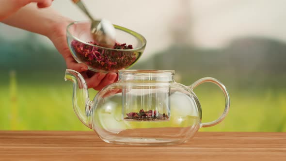 Putting Dry Tea Leaves Into Teapot on a Wooden Table