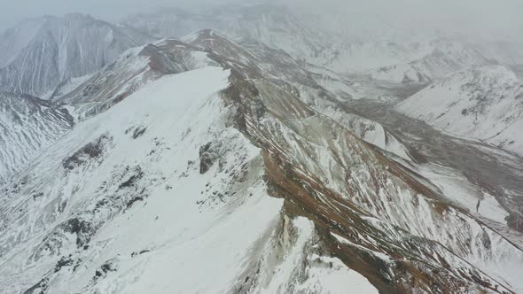 Drone Flight Over Mountain Peaks With Snow Covering One Side