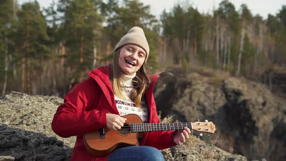 Woman Sits on Rock and Plays the Ukulele