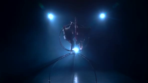 Gymnasts in Suit Performs a Trick on the Aerial Hoop Metal Construction. Black Smoke Background