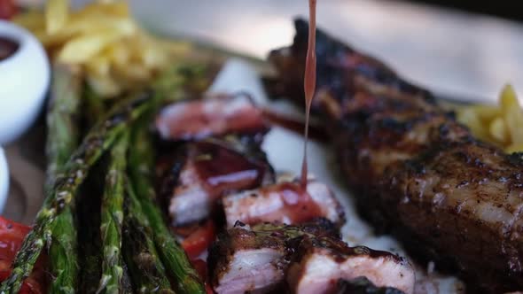 Pouring Tomato Sauce on Beef or Pork Grilled Ribs Served with Aspargus and French Fries on a Wooden