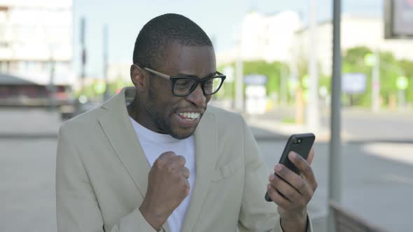 African Man Celebrating Online Success on Smartphone Outdoor