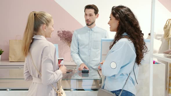 Friendly Male Cashier Accepting Smartphone Payment Giving Shopping Bags to Clients Smiling