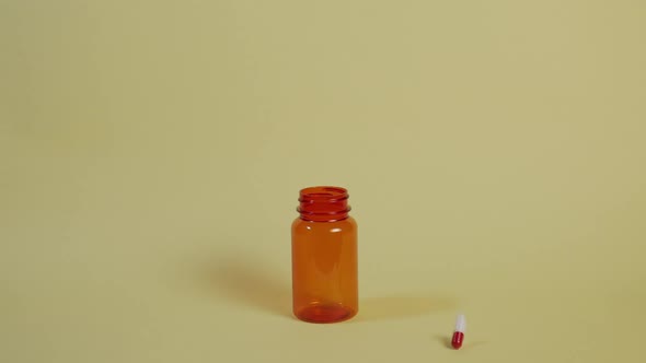 Slow motion wide shot of a pill as it falls vertically towards an open pill bottle and bounces off t