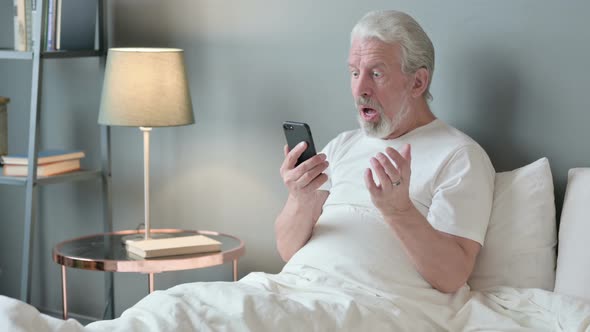 Failure, Old Man Reacting To Loss on Smartphone in Bed 