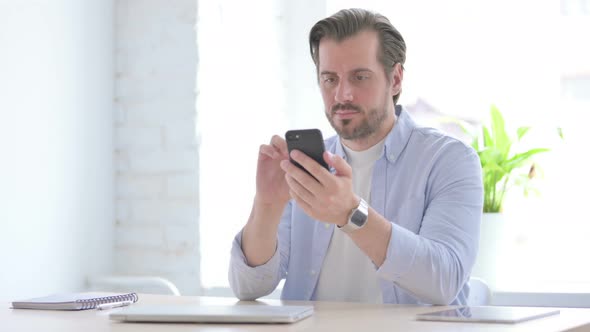 Successful Young Man Celebrating on Smartphone in Office