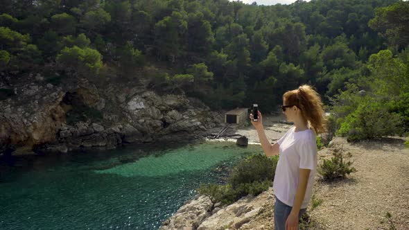 Smiling redheaded woman making a video of a bay, Ibiza