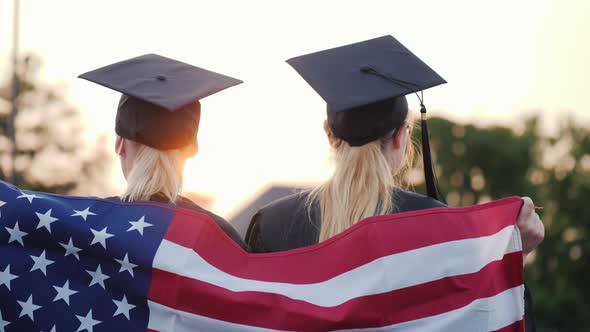 Two Women College Graduates with America Flag on Shoulders, Rear View