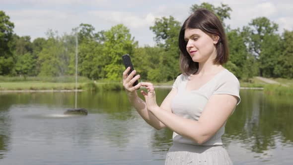 A Young Caucasian Woman Works on a Smartphone in a City Park on a Sunny Day