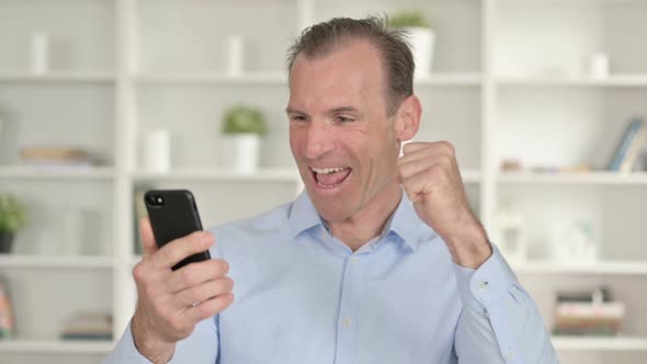 Portrait of Middle Aged Businessman Celebrating Success on Smartphone