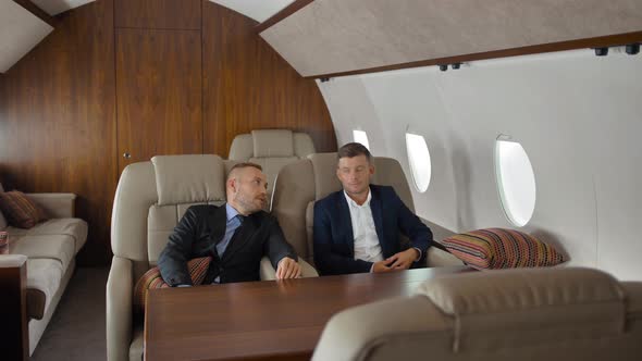 Young Businessmen Talking, Sitting in Airplane Interior During Flight.