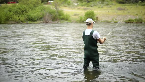 Slow Motion Shot of a Caucasian male fisherman casting his hook while Fly Fishing. He is standing in