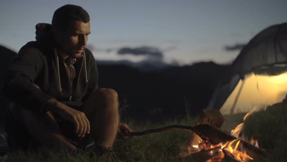 Young Man Warming with Camp Fire in Nature Mountain Outdoor Camping Scene at Night Dolly