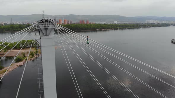 A Man Walks on a Rope Stretched Between the Supports of the Bridge at High Altitude. alt