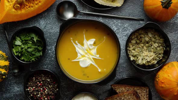 Delicious Pumpkin Soup with Cream, Seeds, Bread and Fresh Herbs in Elegant Ceramic Black Bowl