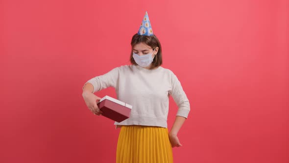 Optimistic Girl with Medical Mask on Face and Cone on Head Giving Gift Box