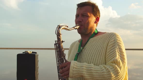 Portrait of a Man Playing Saxophone Outdoors in the Sea, Sunset Sky 