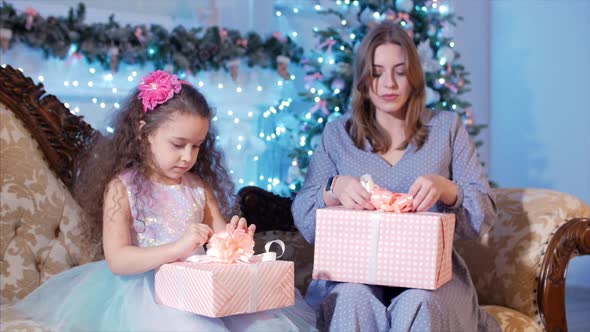 Young Happy Mother With Her Little Sweet Daughter Open a Gifts, Look Inward and Rejoice in the
