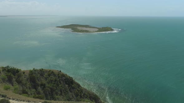 Epic flying off the side of a cliff towards an amazing tropical island as bird flies in front of cam