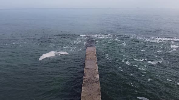 Aerial view drone flies over the sea along a concrete pier.