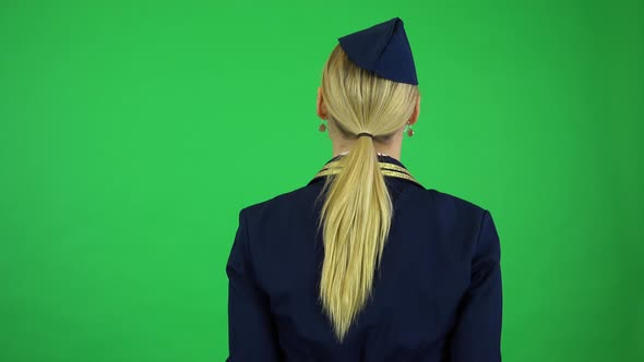 A Young Beautiful Stewardess Shows Exit Ways on a Plane To the Camera - Green Screen Studio