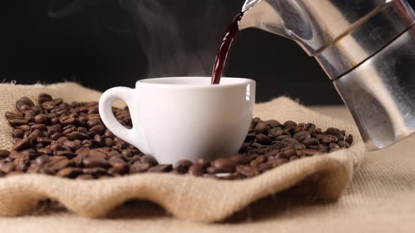 Pouring hot steaming coffee on cup from moka coffee machine. Jute background and coffee beans