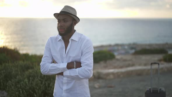 Sad African American Gay Man Standing on Mediterranean Sea Coast at Sunset with Crossed Hands