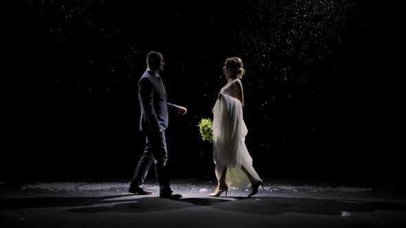 Happy Newlywed Couple Approach Each Other Against the Background of Falling Snow. A Man in a Suit